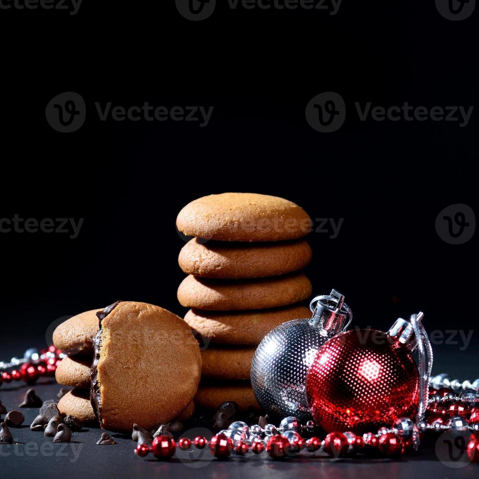 Kekse - Stapel köstlicher Sahnekekse gefüllt mit Schokoladencreme, verziert mit Weihnachtsschmuck auf schwarzem Hintergrund foto