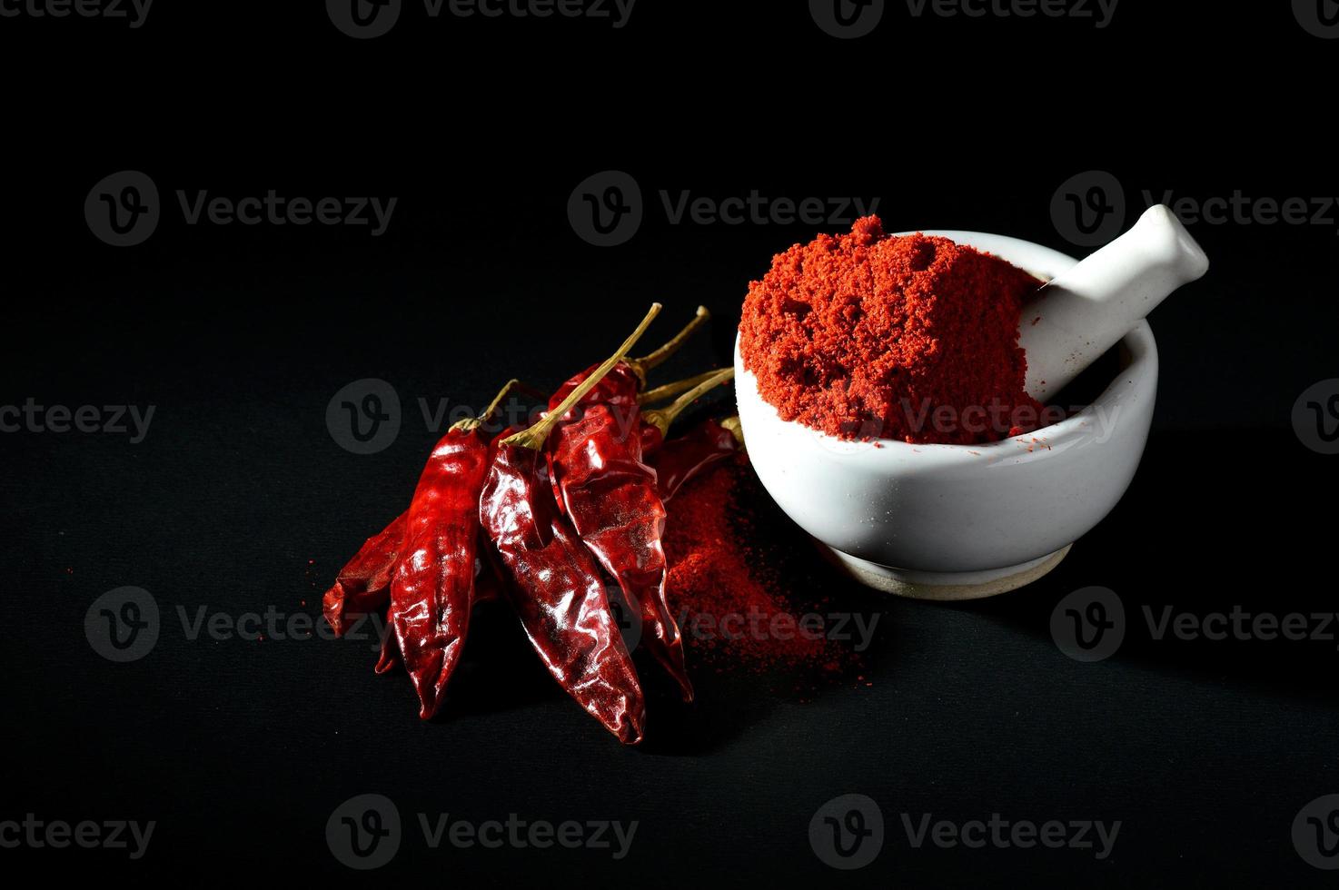 rotes Chilipulver im Stößel mit Mörser und rote Chilischoten auf schwarzem Hintergrund foto