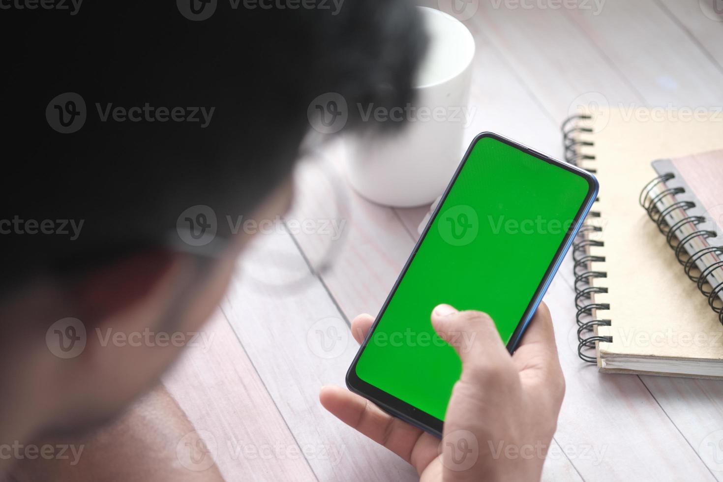 Rückansicht der Hand des jungen Mannes mit Smartphone mit grünem Bildschirm foto