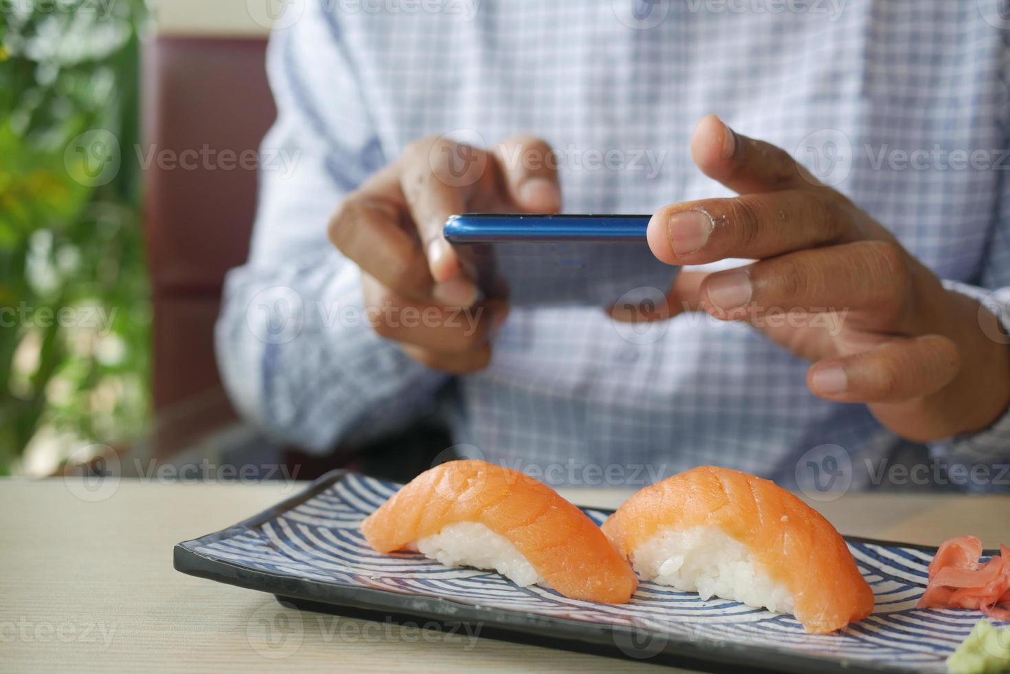 junger Mann, der mit dem Telefon ein Foto von japanischem Nigiri-Sushi-Lachs macht