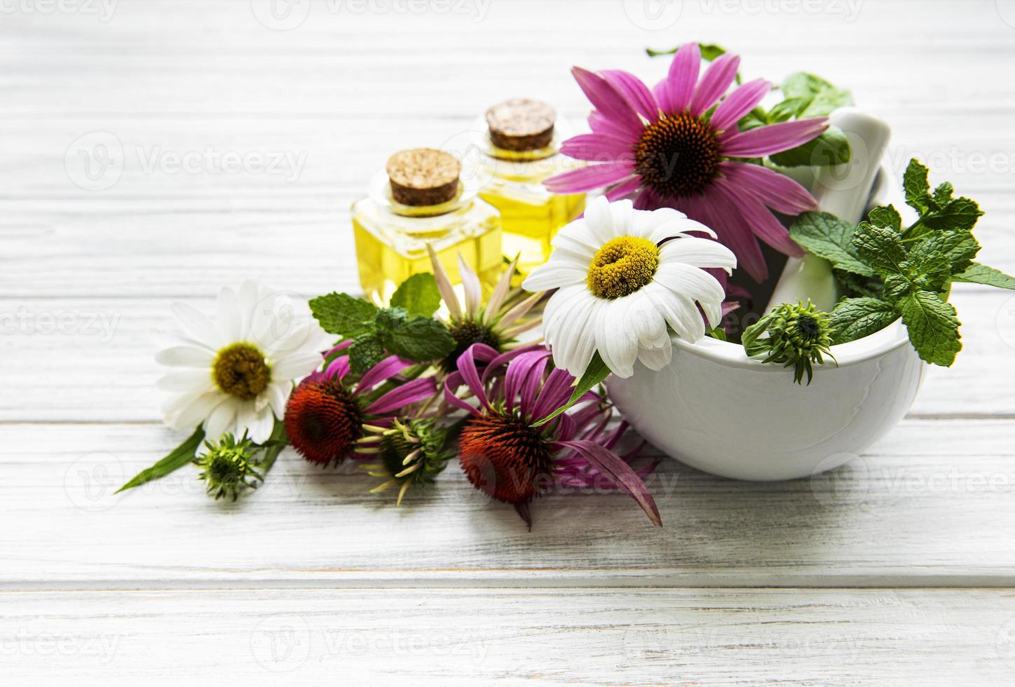 medizinische Blumen und Pflanzen in Mörser und ätherischen Ölen auf einem weißen Holztisch foto