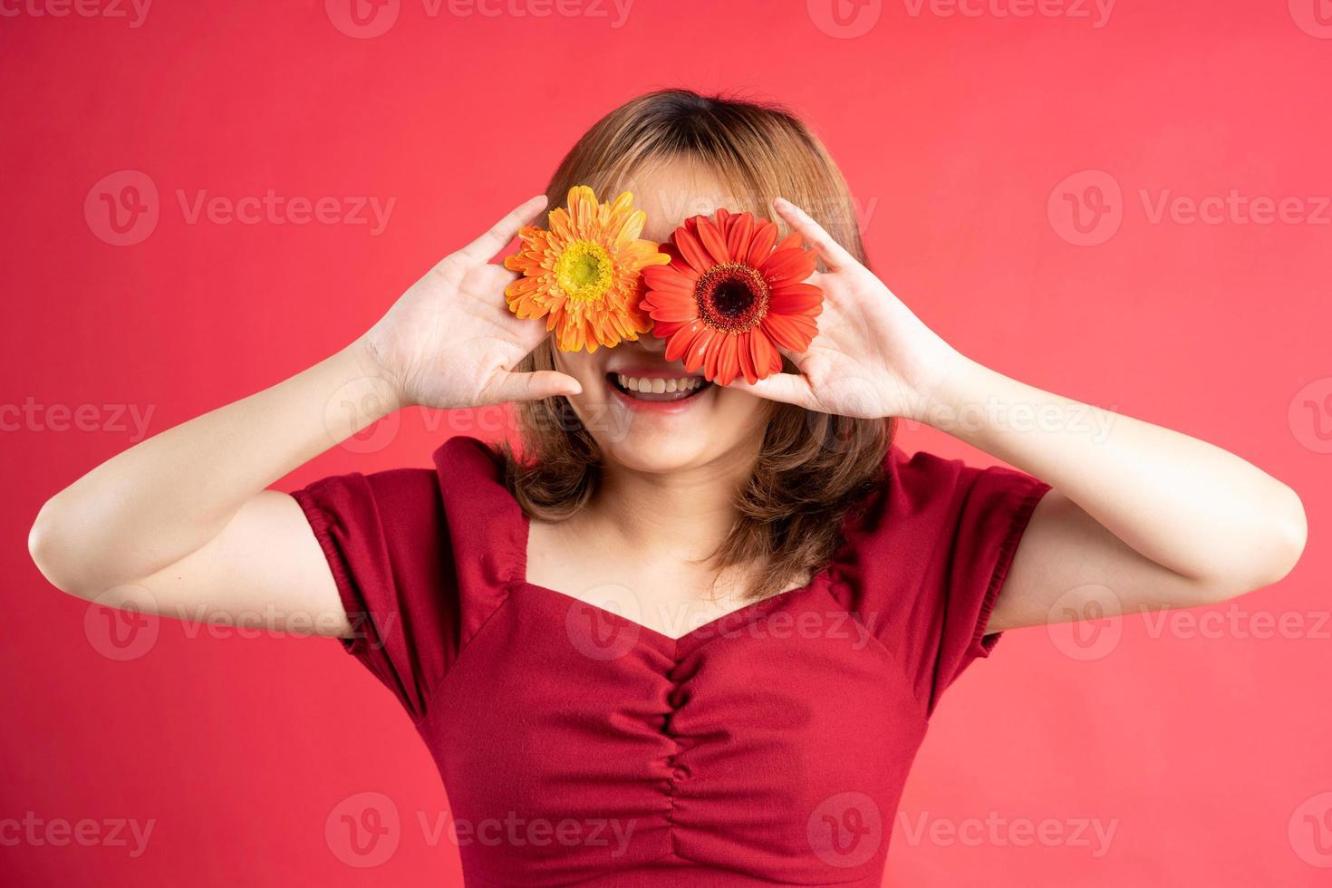 junges Mädchen, das rote und gelbe Blume über ihren Augen hält foto