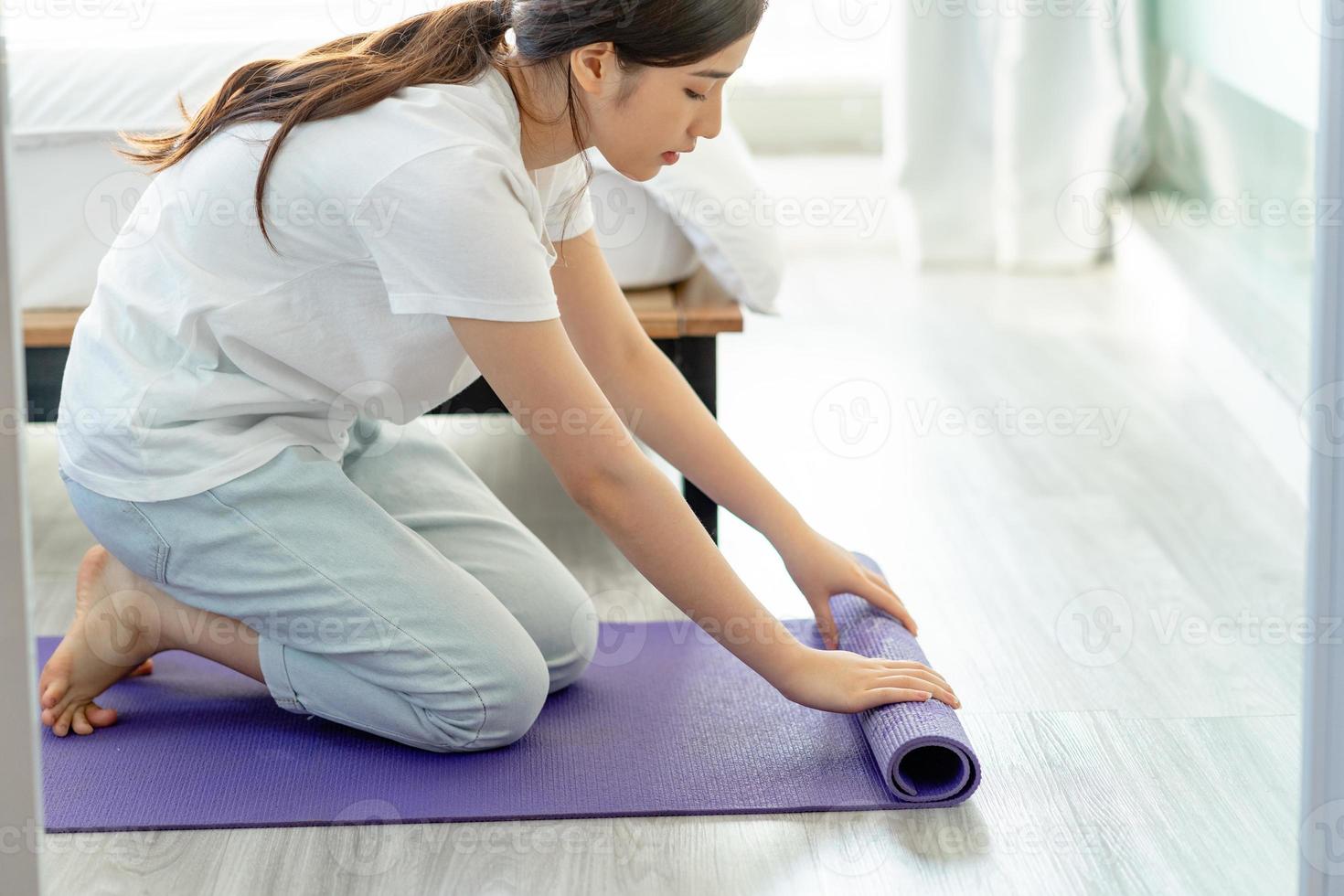 asiatische Frau, die Yogamatte ausbreitet, um Yoga zu Hause vorzubereiten foto