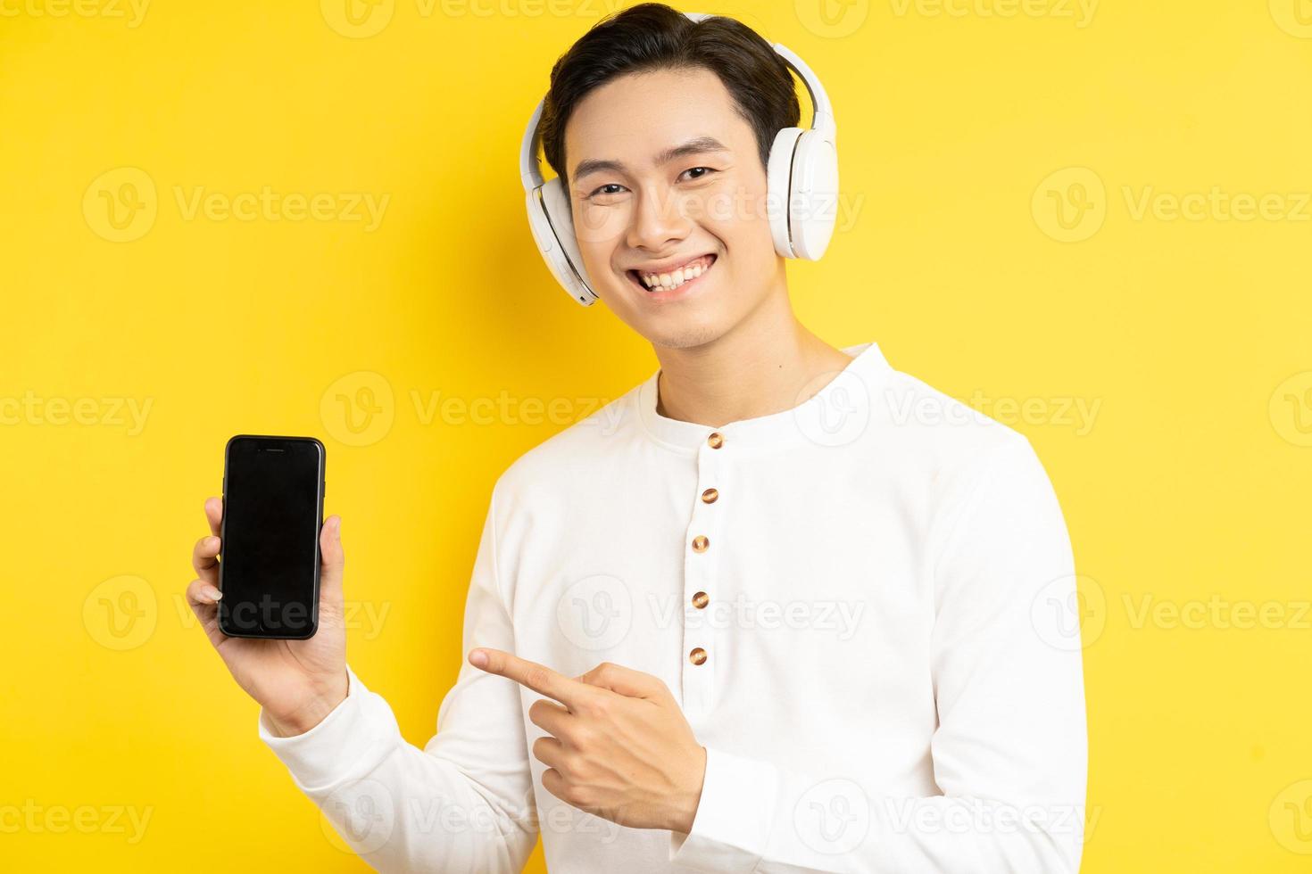 Der asiatische Geschäftsmann trug drahtlose Kopfhörer, um Musik zu hören, und sein Finger zeigte auf das Handy, das er hielt foto