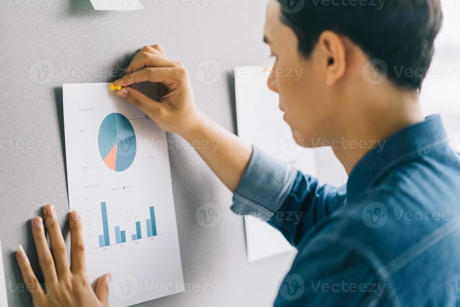 Asiatischer Geschäftsmann klebt das Diagramm an die Tafel, um sich auf die Präsentation vorzubereiten foto