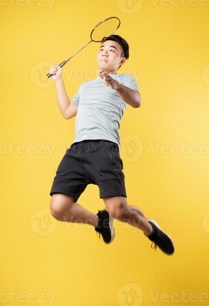 asiatischer Mann, der Badminton auf gelbem Hintergrund spielt foto