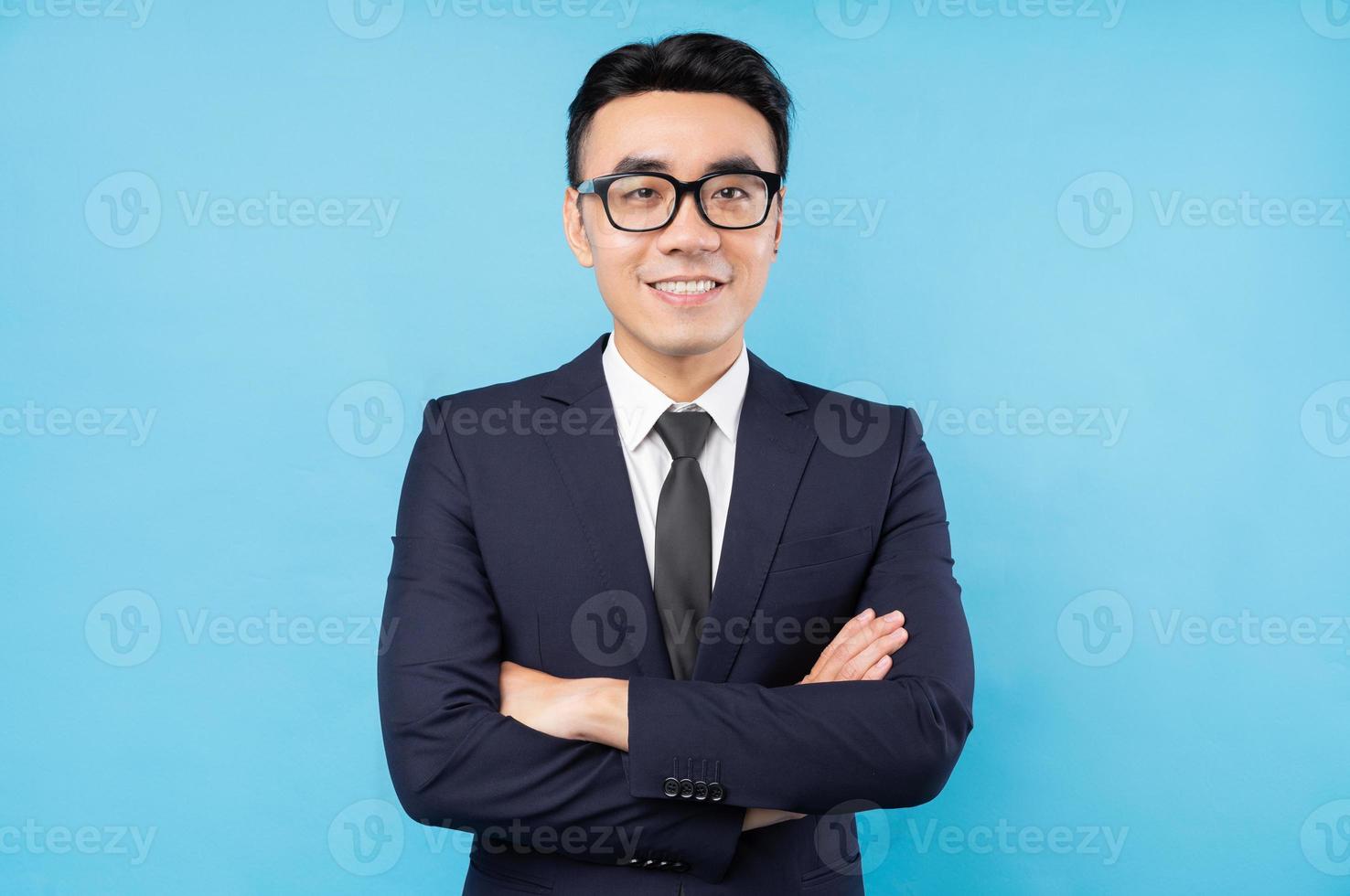 Porträt eines asiatischen Geschäftsmannes mit verschränkten Armen und lächelnd auf blauem Hintergrund foto