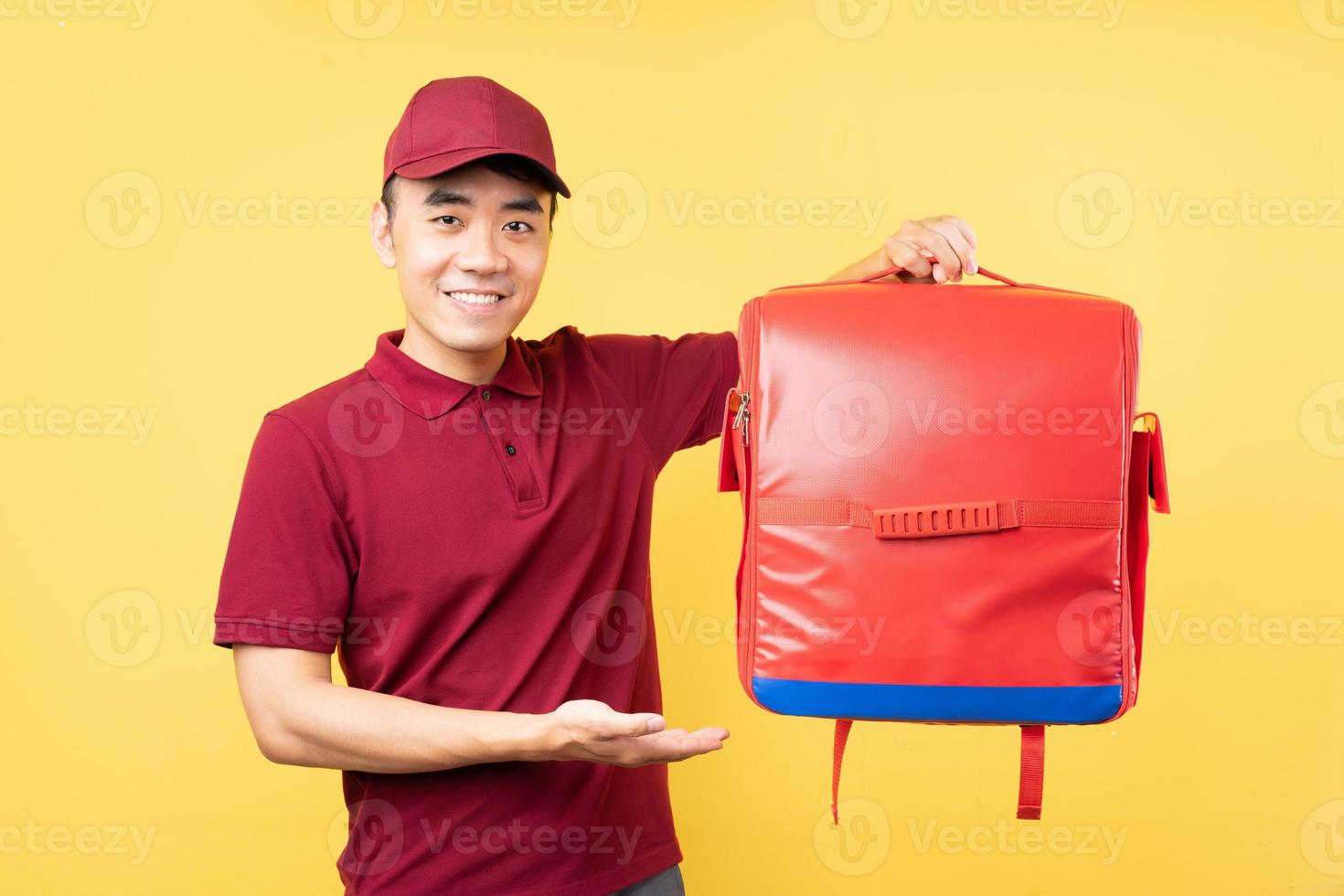 asiatischer Lieferbote, der eine rote Uniform trägt, die auf gelbem Hintergrund posiert foto
