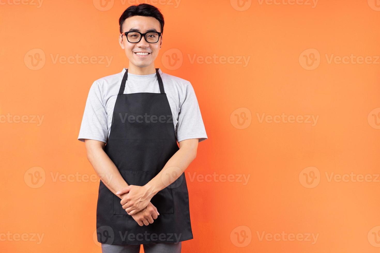 Porträt des asiatischen männlichen Kellners, der auf orangem Hintergrund posiert foto