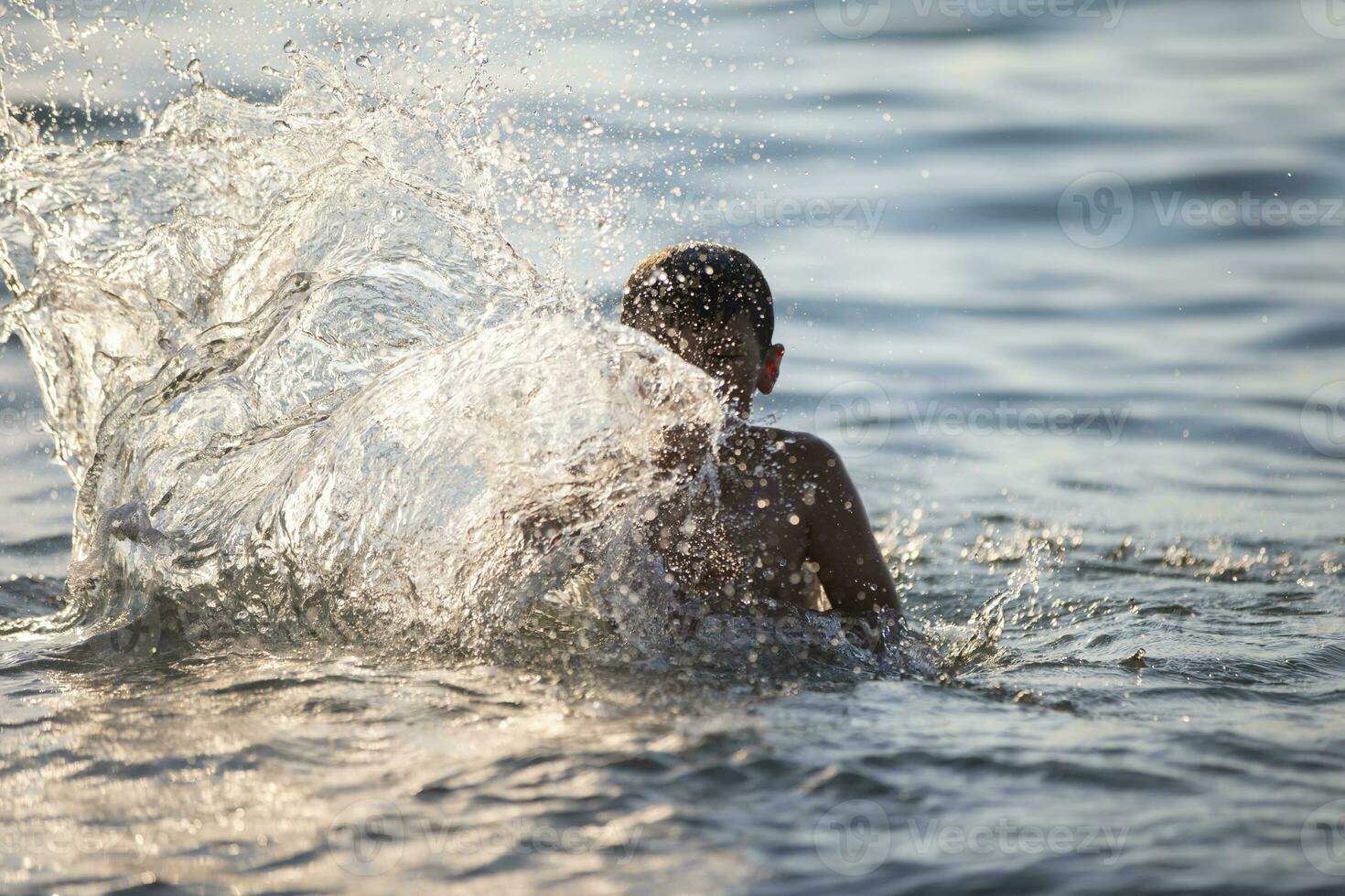 glücklich Teen Junge Theaterstücke mit Meer Wellen. das Junge schwimmt im das Meer. foto