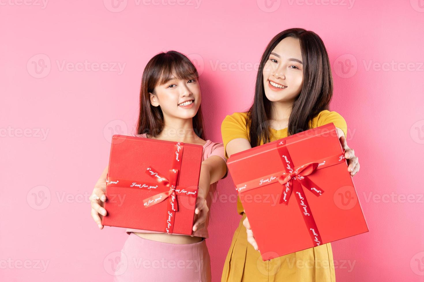 Porträt von zwei schönen jungen asiatischen Mädchen, die eine rote Geschenkbox auf rosa Hintergrund halten foto