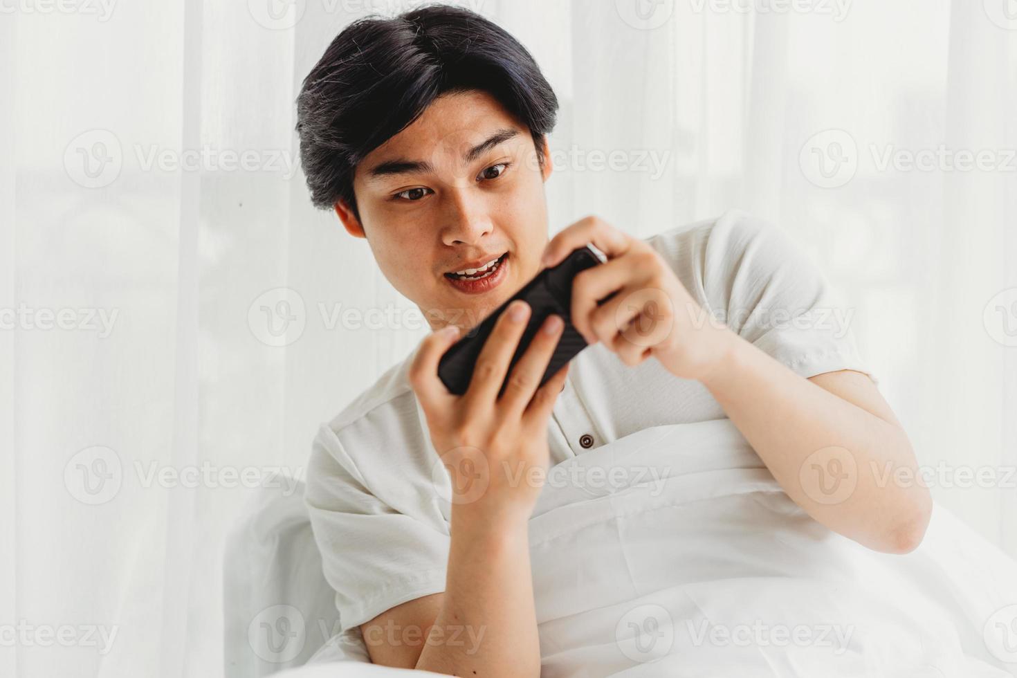 asiatischer Mann benutzt sein Handy, um Spiele im Bett zu spielen foto