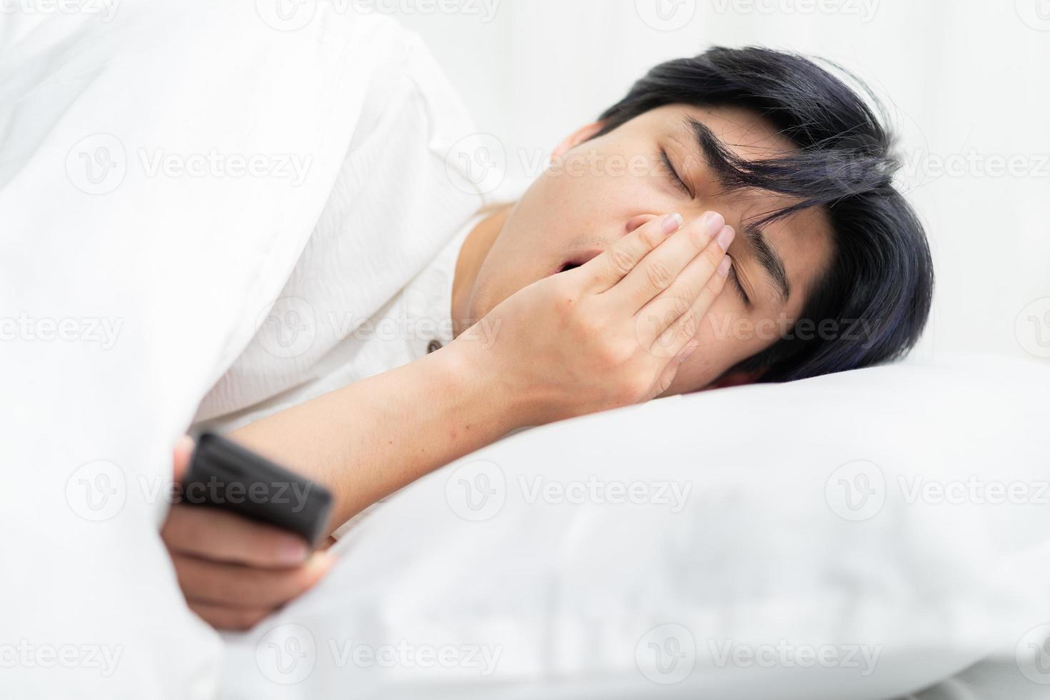 asiatischer Mann, der im Bett liegt und das Telefon benutzt. schläfrig beim Telefonieren foto
