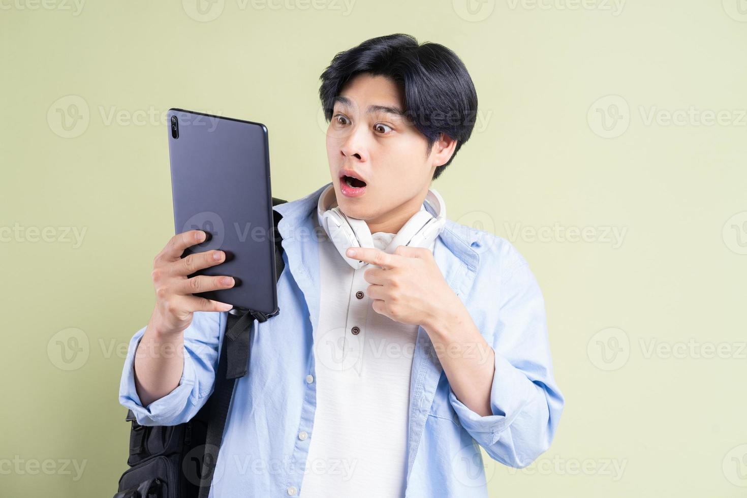 männlicher asiatischer Student zeigt mit einem überraschten Gesicht mit dem Finger auf das Tablet foto