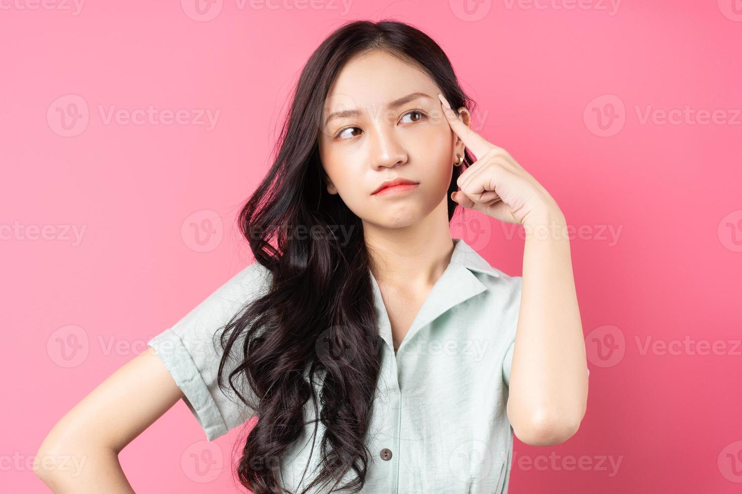 junge asiatische frau, die über einen rosa hintergrund nachdenkt foto