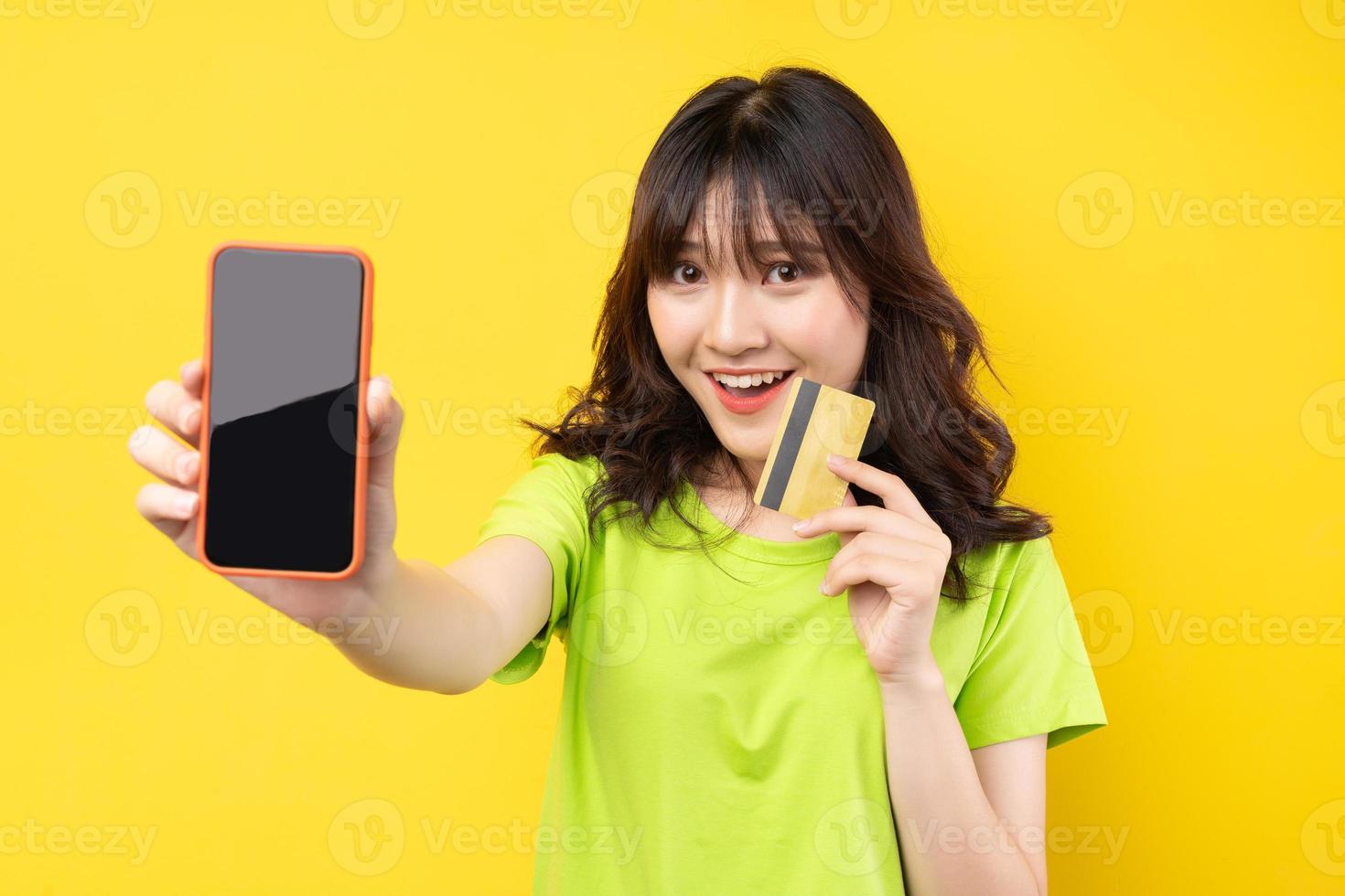 junges Mädchen, das Telefon und Kreditkarte mit fröhlichem Ausdruck im Hintergrund hält foto