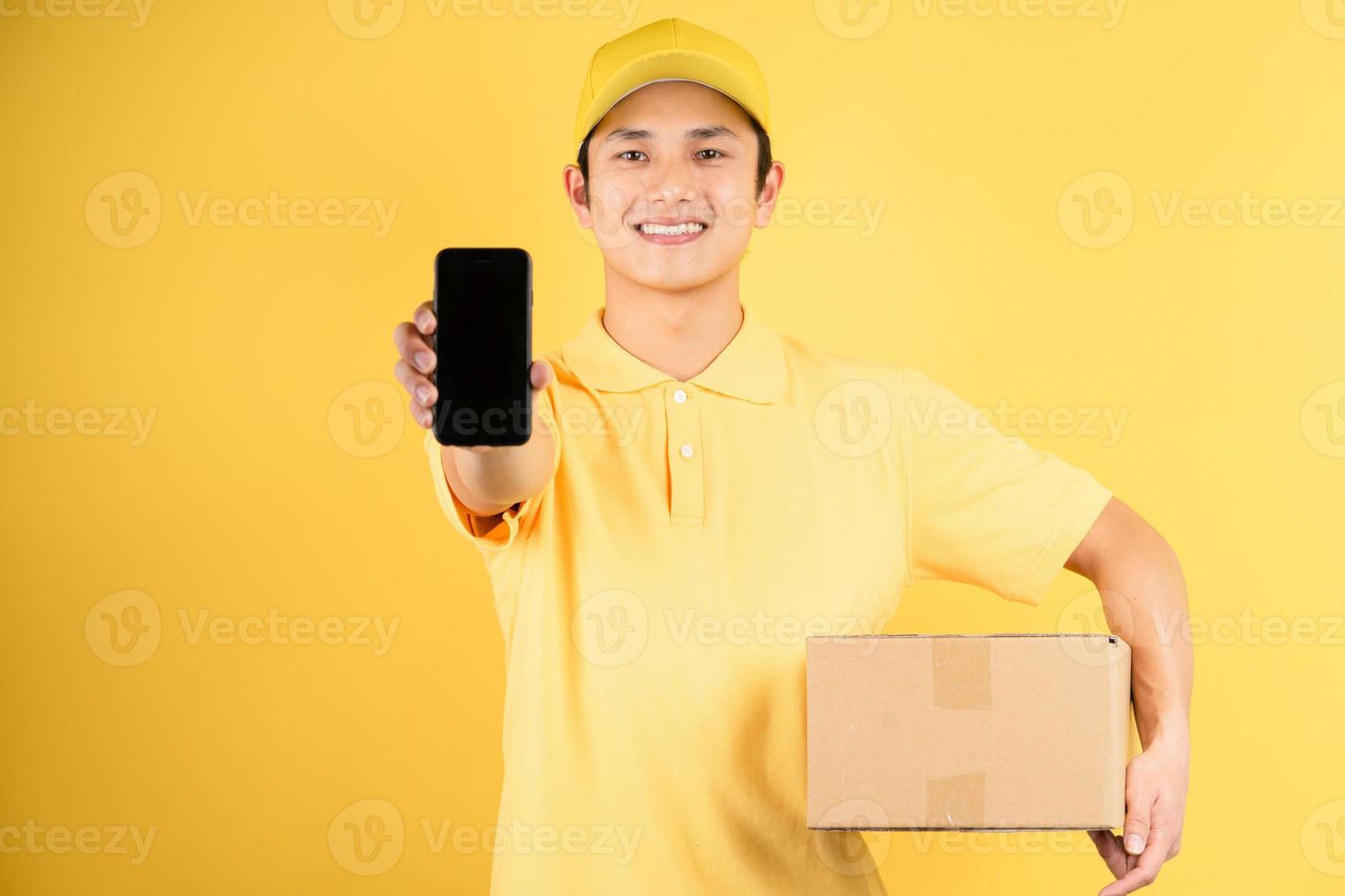 Lieferung männliches Porträt, das Frachtbox hält und Telefon auf gelbem Hintergrund hält foto