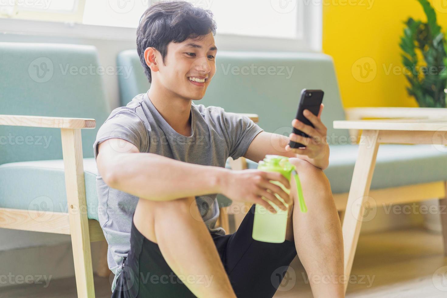 asiatischer Mann, der sich nach dem Training ausruht und das Telefon benutzt foto