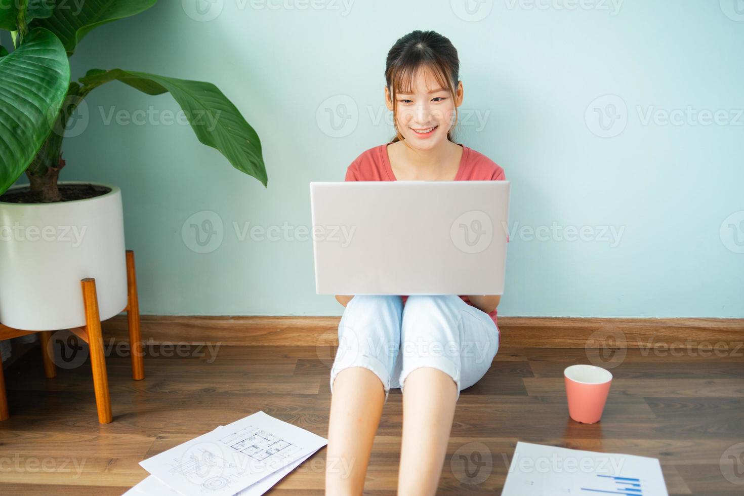 asiatische frau, die auf dem boden sitzt, während sie von zu hause arbeitet foto