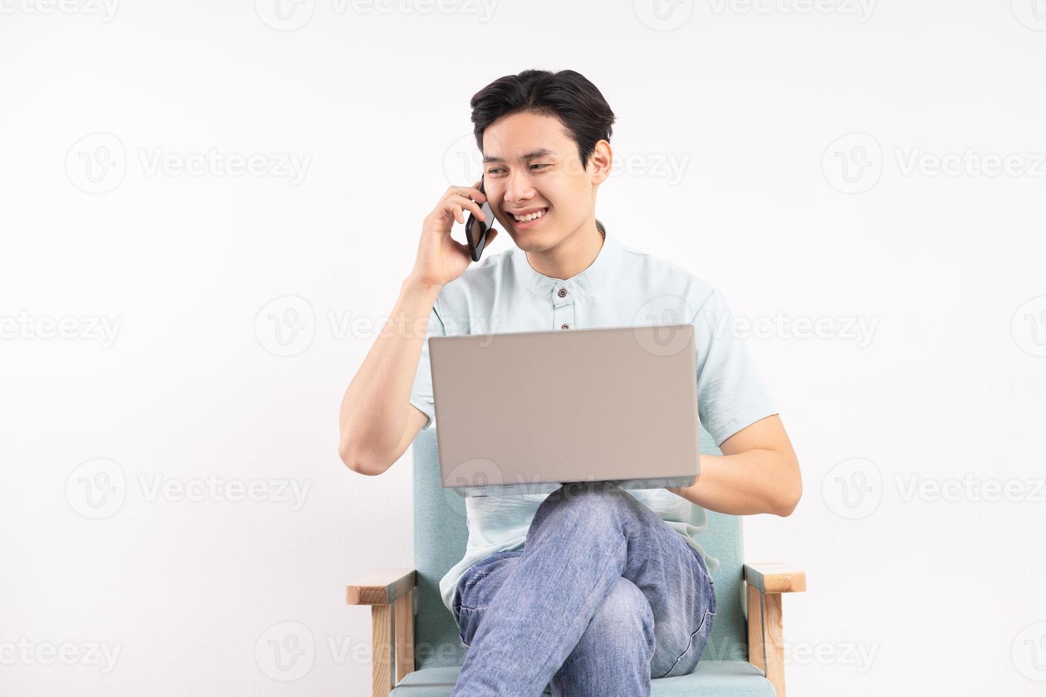 Gut aussehender Mann mit Laptop, der auf dem Sofa sitzt, das Telefon hört und arbeitet foto