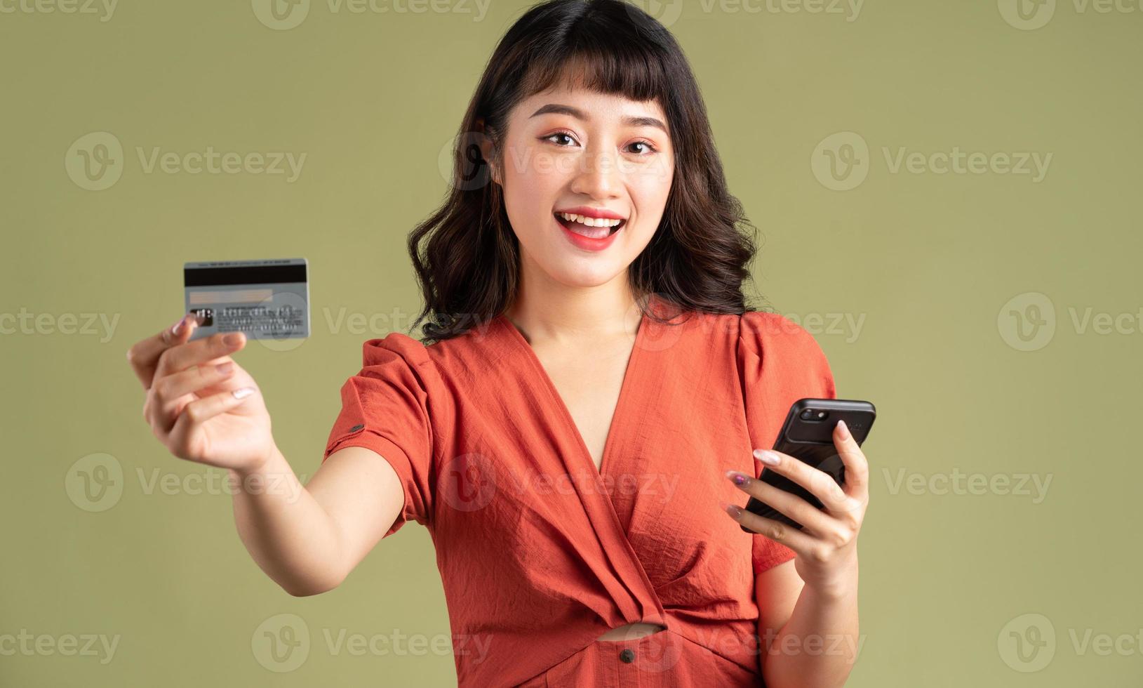 asiatische Frau, die eine Bankkarte hält und auf ihr Telefon starrt foto