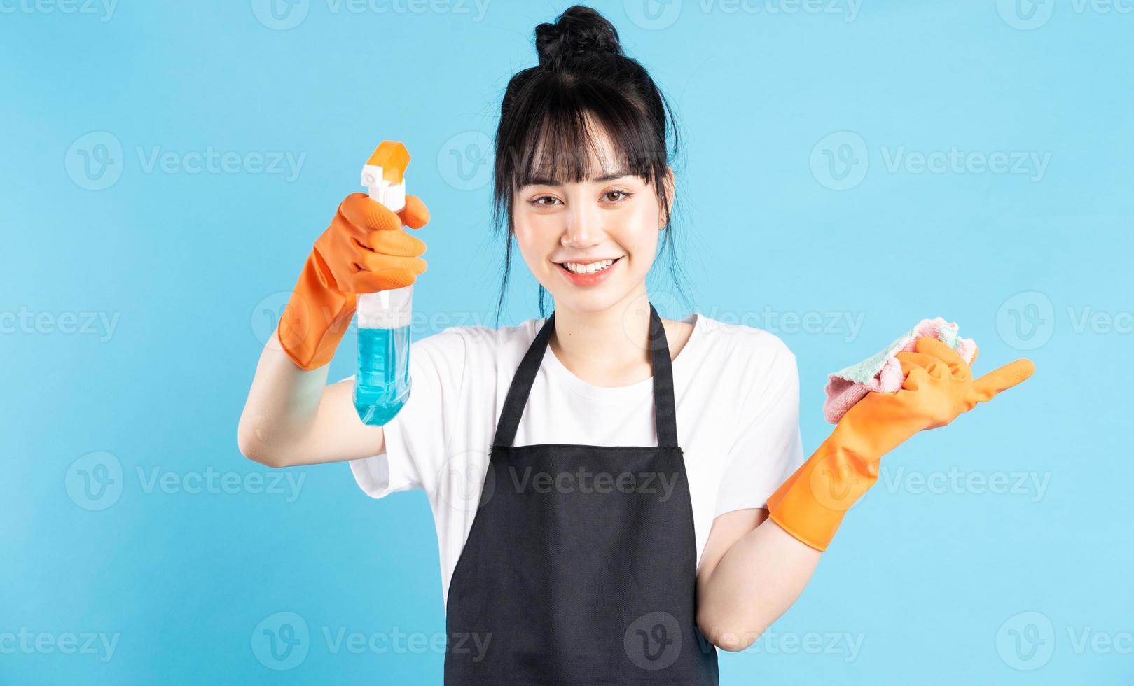 asiatische Hausfrau trägt orangefarbene Handschuhe und hält einen Wasserstrahl in der Hand foto