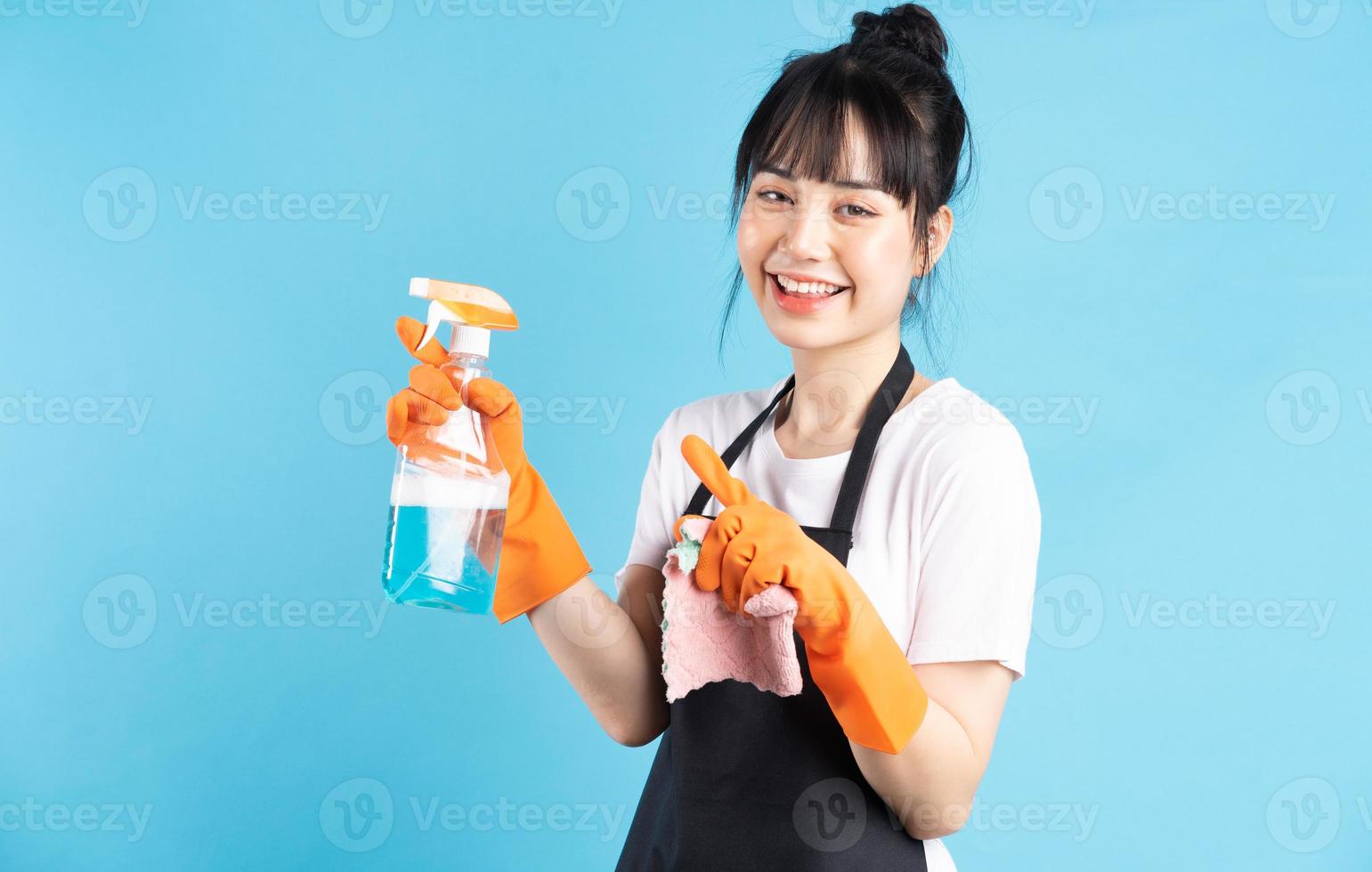 asiatische Hausfrau trägt orangefarbene Handschuhe und hält einen Wasserstrahl in der Hand foto