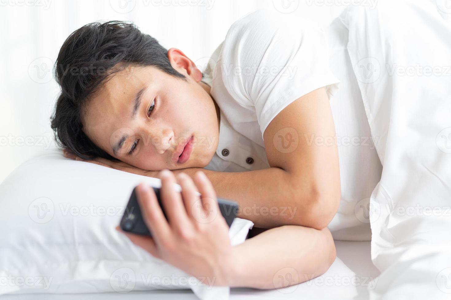 junger Mann liegt mit einem Telefon im Bett foto