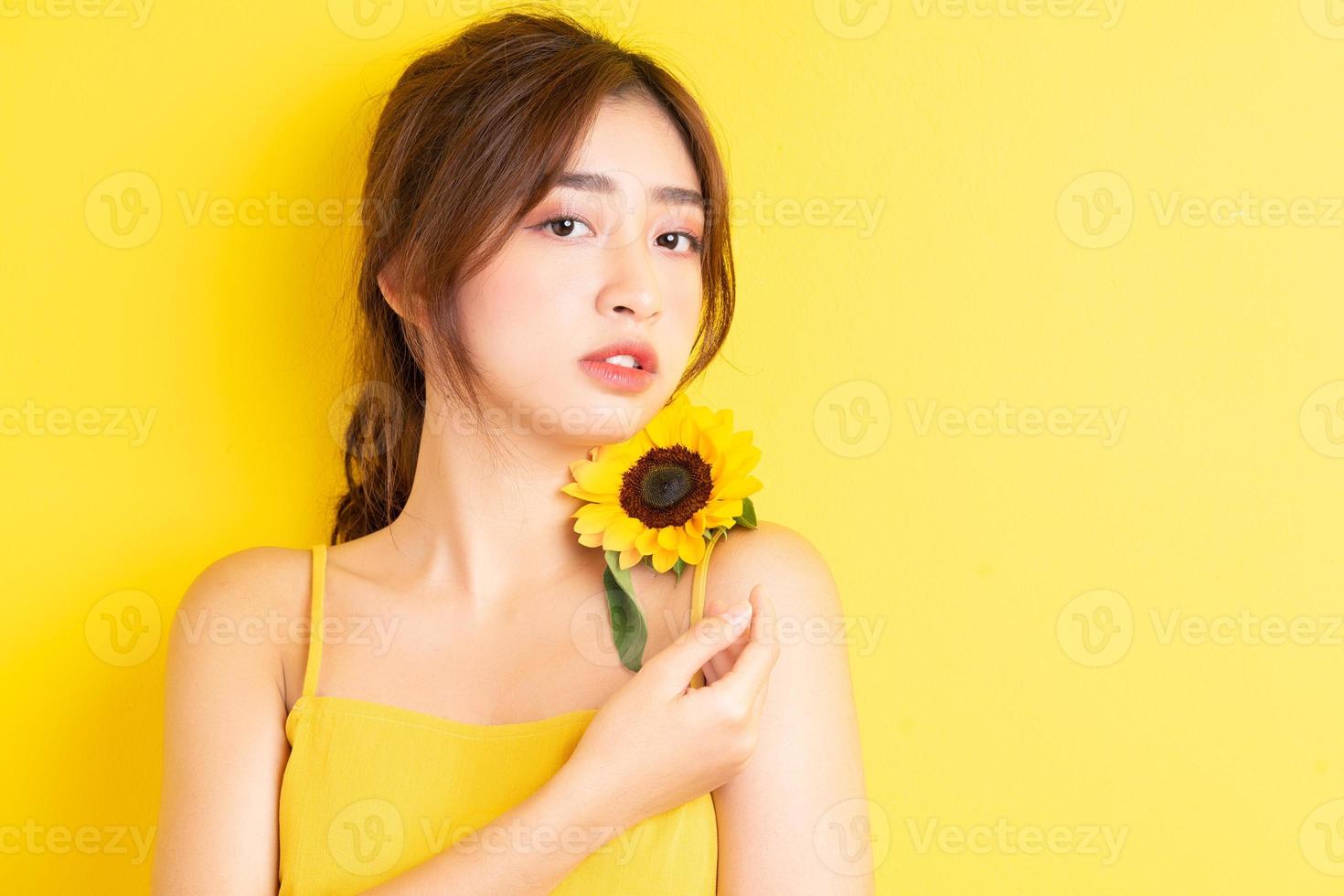 schöne asiatische frau, die mit sonnenblume auf gelbem hintergrund hält und posiert foto