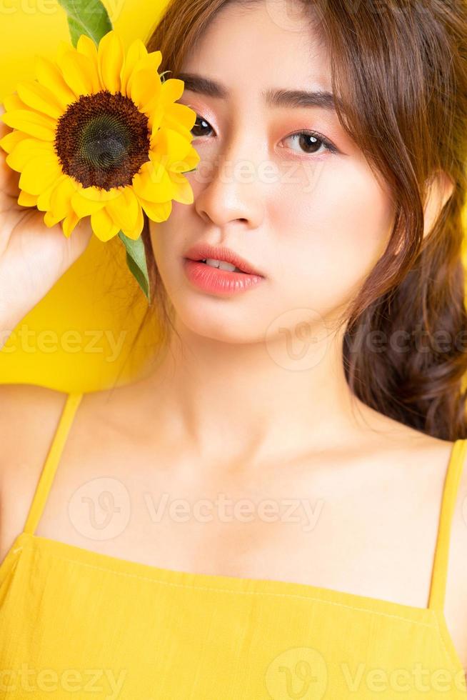 schöne asiatische frau, die mit sonnenblume auf gelbem hintergrund hält und posiert foto