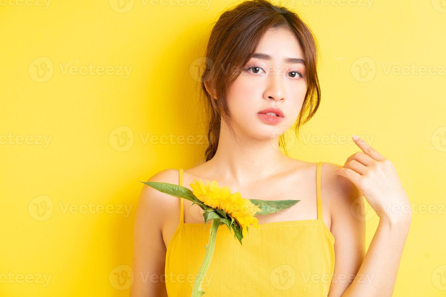 schöne asiatische frau, die mit sonnenblume auf gelbem hintergrund hält und posiert foto