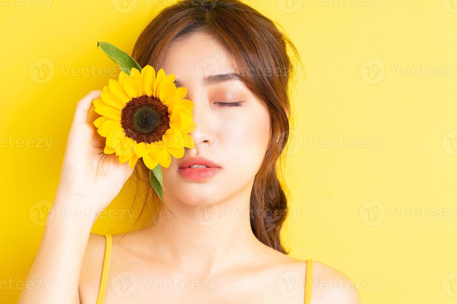 schöne asiatische frau, die mit sonnenblume auf gelbem hintergrund hält und posiert foto