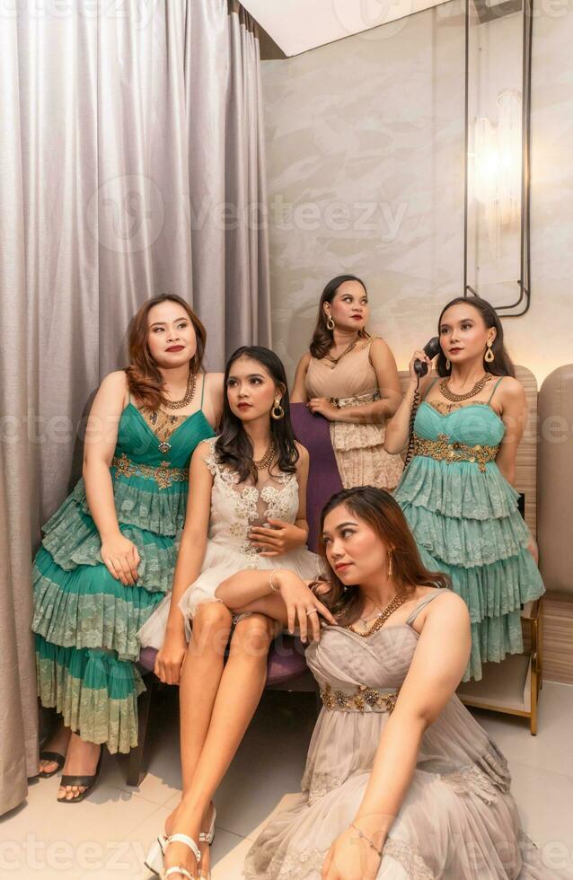 ein Gruppe von asiatisch Frauen im glamourös und luxuriös Kleider sind Sitzung auf das Sofa mit ihr freunde nach Party machen foto