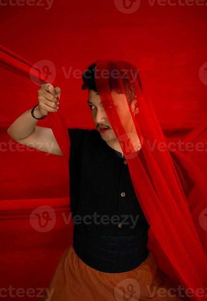 ein asiatisch Mann im ein schwarz Hemd Abdeckung seine Gesicht mit ein rot Stoff mit ein erschreckend Gesichts- Ausdruck im Vorderseite foto