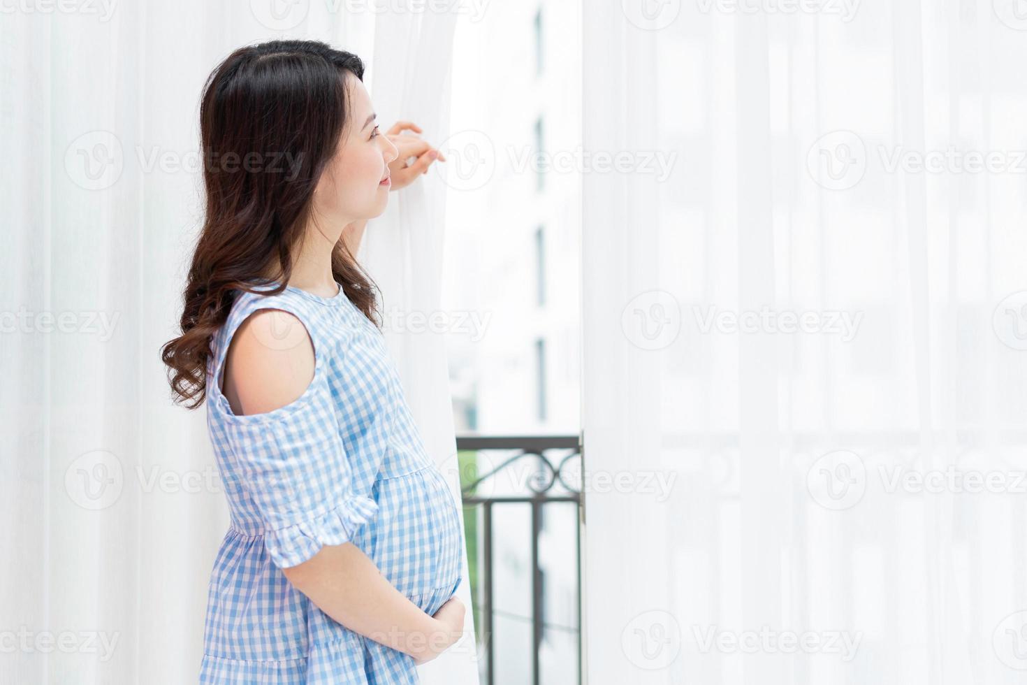 schöne frau, die ihren schwangeren bauch am fenster hält foto