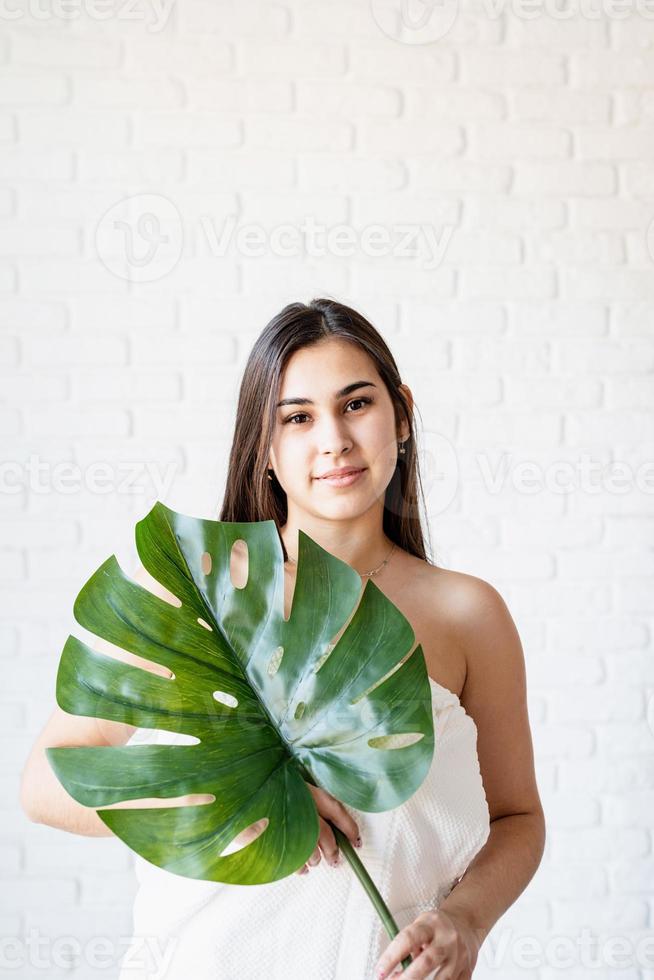 glückliche schöne Frau mit Badetüchern, die ein grünes Monstera-Blatt vor ihrem Gesicht hält foto