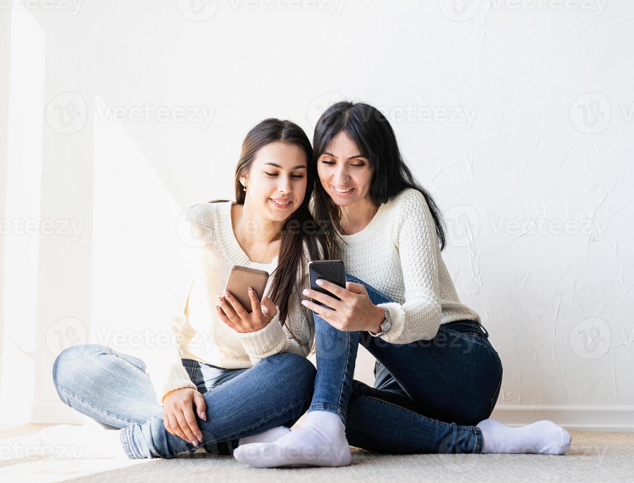 Zwei schöne Freundinnen senden Nachrichten mit Mobiltelefonen foto