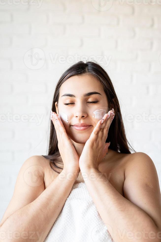 glückliche schöne Frau trägt Bademäntel, die Gesichtscreme auf ihr Gesicht aufträgt foto