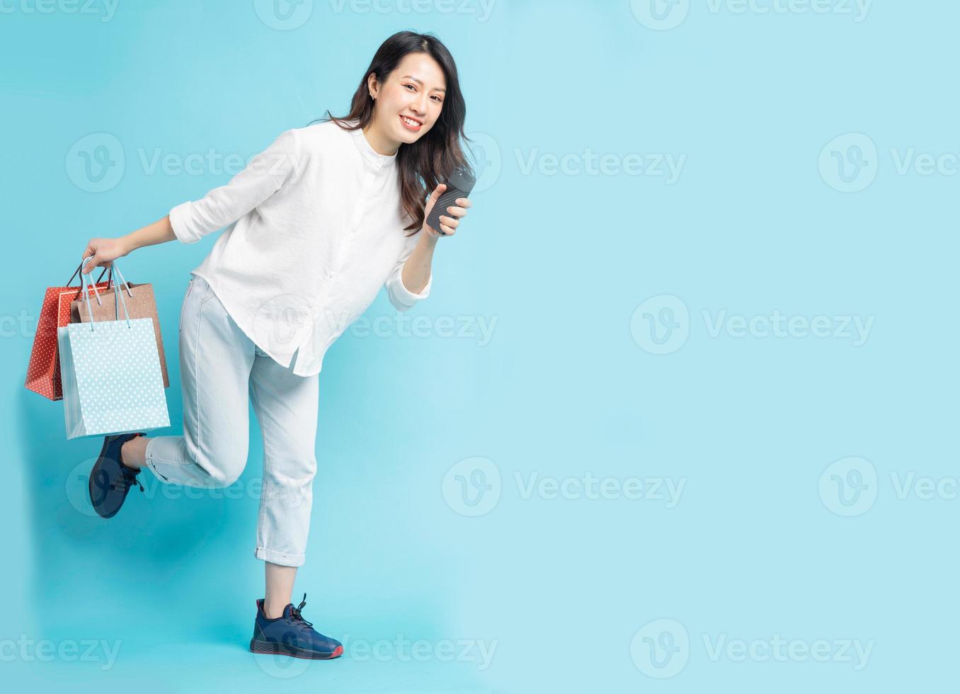 schöne asiatische frau mit einkaufstaschen und telefon in der hand beim laufen foto