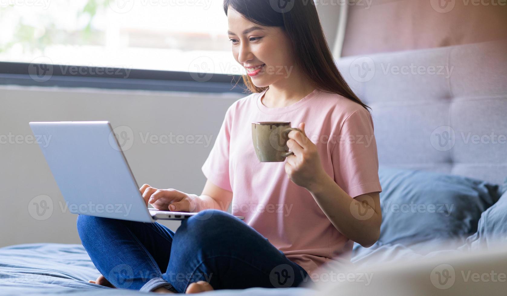 schöne junge asiatische frau, die im bett sitzt und computer benutzt foto