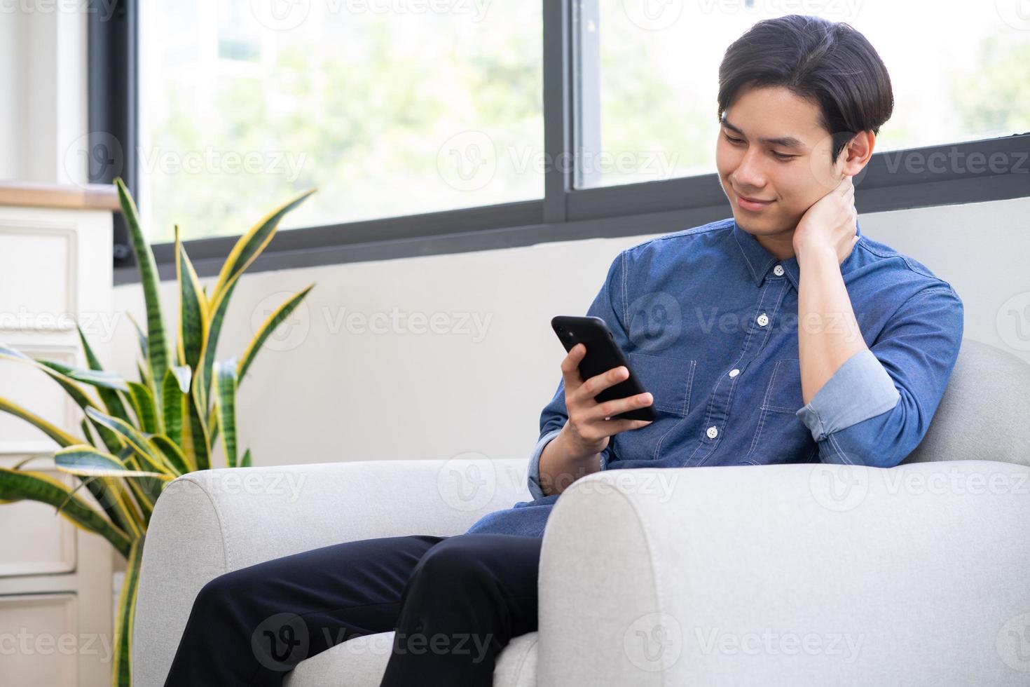 junger asiatischer mann, der das telefon im wohnzimmer benutzt foto