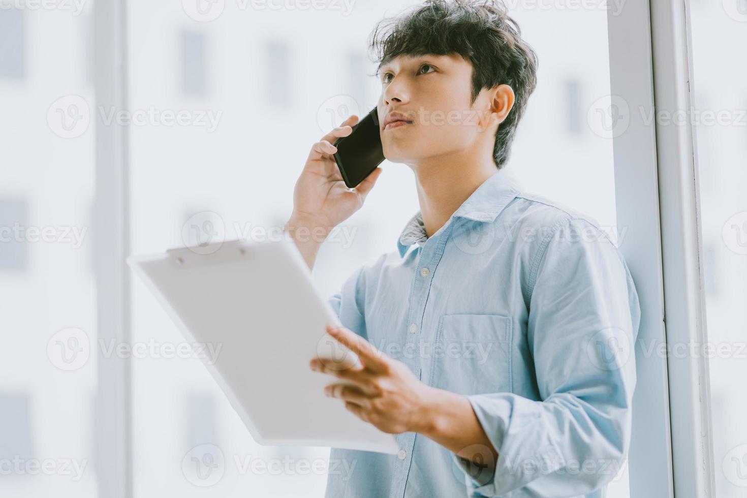 Asiatischer Geschäftsmann ruft an, um über die Arbeit am Fenster zu diskutieren by foto