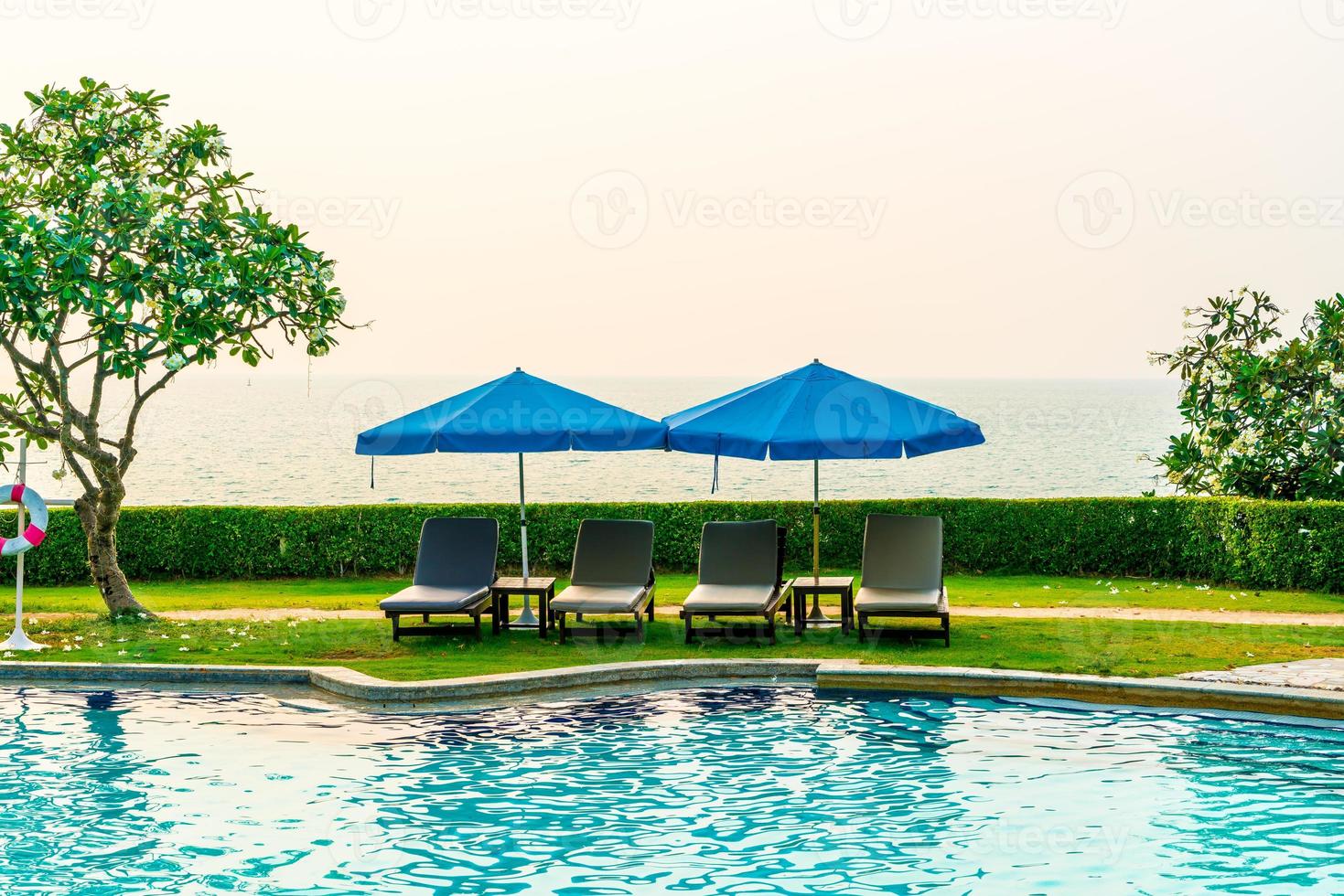 Liegestühle oder Poolbetten mit Sonnenschirmen um den Pool bei Sonnenuntergang foto