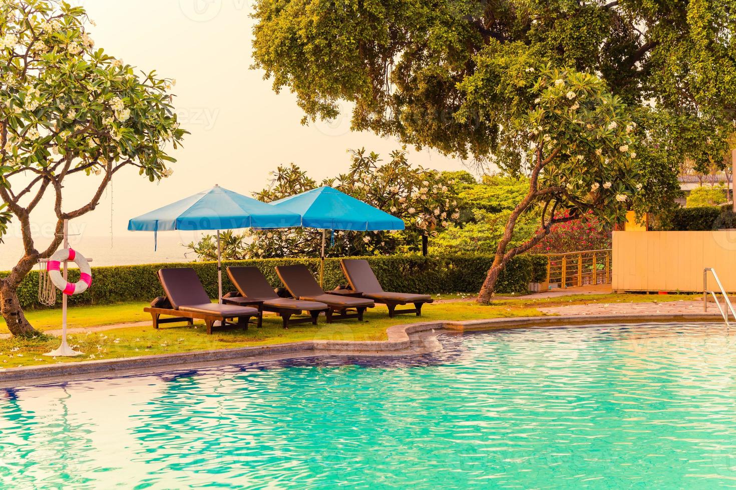 Liegestühle oder Poolbetten mit Sonnenschirmen um den Pool bei Sonnenuntergang foto