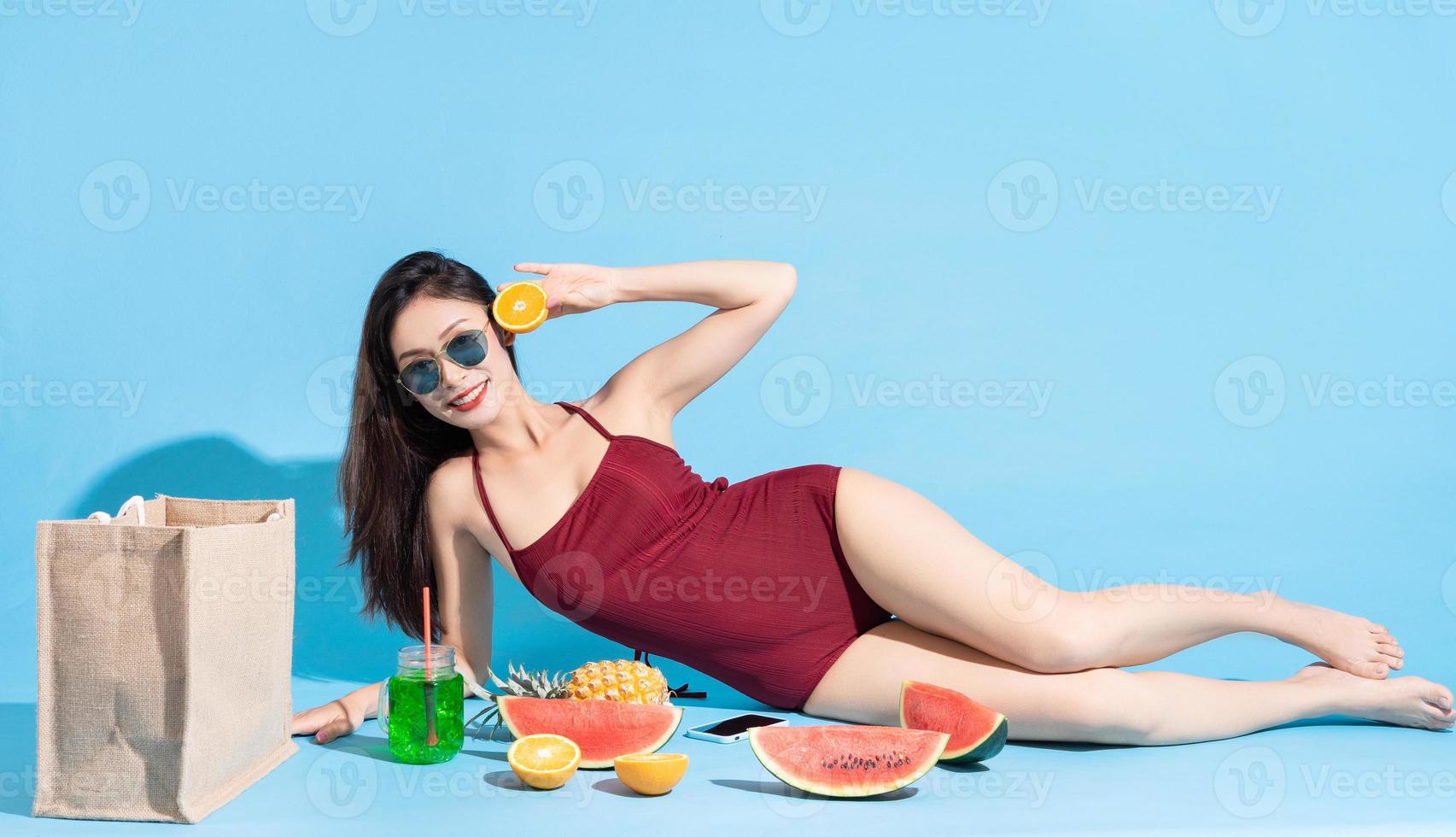 asiatische Frau im roten Badeanzug mit tropischen Früchten auf blauem Hintergrund foto