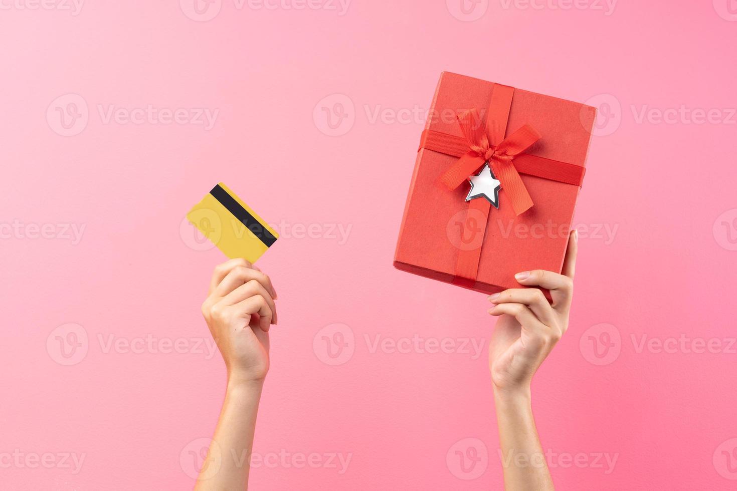 Hände, die rote Geschenkbox und Bankkarte auf rosa Hintergrund halten foto