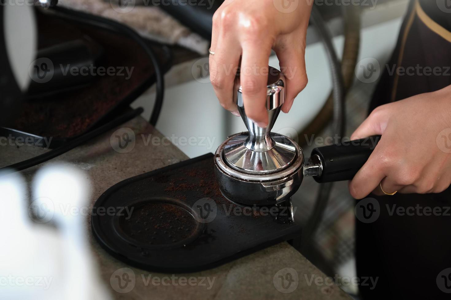 Eine Arbeiterin presst geröstete Kaffeebohnen mit einer Tamperstange, bevor sie in die Kaffeemaschine gegeben werden foto