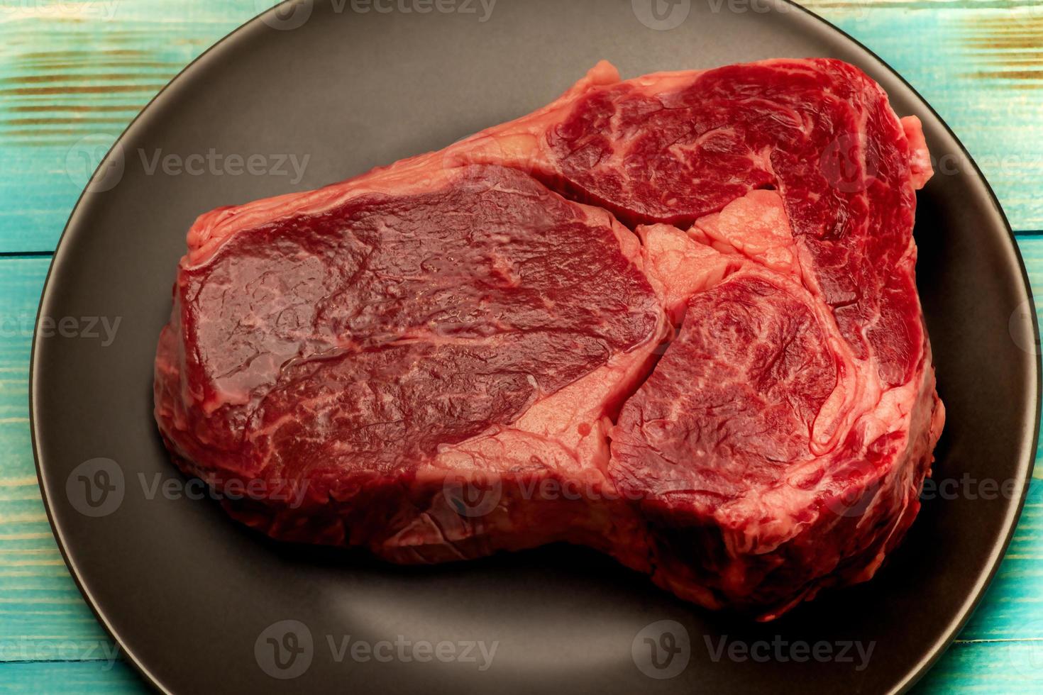 Steak-Kochprozess. das Fleisch ist in einem schwarzen Teller. ein Stück rohes Rindfleisch auf einem Teller. foto