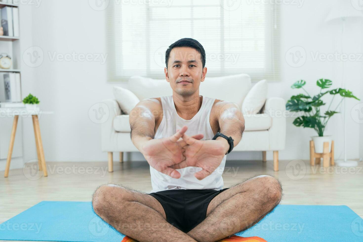 online Klasse Ausbildung. asiatisch reifen Mann Dehnen im Sportbekleidung Herstellung Dehnen zum Beine auf Matte Yoga im Leben Zimmer Innere und lächelnd. glücklich Sportler trainieren durch ihm slef. Sport beim heim. foto