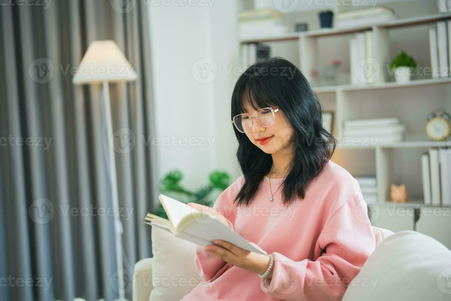 froh glücklich asiatisch Frau lächelnd und lesen Buch während Sitzung auf Couch Sofa im Leben Zimmer beim heim. asiatisch Frauen entspannen lesen Buch Lächeln beim Sofa im das Haus. Aktivität Hobby beim Haus Konzept. foto